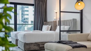 Ein modernes Hotelzimmer mit einem großen Bett, einer Couch und einem Schreibtisch. Ein Fenster bietet Blick auf Gebäude.