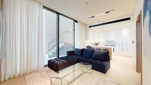 Un salon moderne avec un canapé d’angle, une table basse en verre et une porte-fenêtre coulissante donnant sur la cuisine.