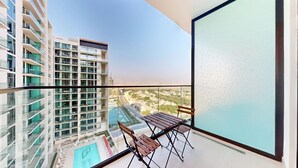 Un balcon avec une table et des chaises, donnant sur une piscine et des immeubles de grande hauteur.