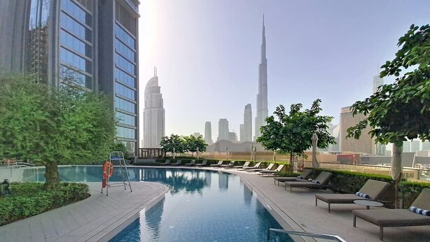 A rooftop pool with lounge chairs and a lifeguard stand, surrounded by greenery and overlooking a cityscape with tall buildings. - 2 Bed Direct Dubai Mall Access l Free Pool, Gym (Downtown Dubai)