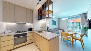 A modern kitchen with built-in appliances, a dining area with a table and chairs, and a living space with a sofa and large windows. - 2 Bed Direct Dubai Mall Access l Free Pool, Gym (Downtown Dubai)