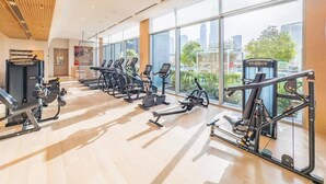 A gym with cardio machines, weight stations, and large windows offering a city view. - 2 Bed Direct Dubai Mall Access l Free Pool, Gym (Downtown Dubai)