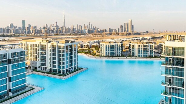 Un complexe résidentiel moderne doté d’une grande piscine, de bâtiments de grande hauteur et offrant une vue sur le panorama urbain en arrière-plan.