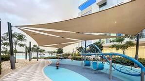 Un espace de jeux pour enfants doté d’une surface en caoutchouc bleu, d’un toboggan et d’une structure d’escalade.