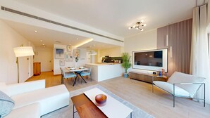 Een moderne woonkamer met een televisie, bank, eettafel en keukenhoek.