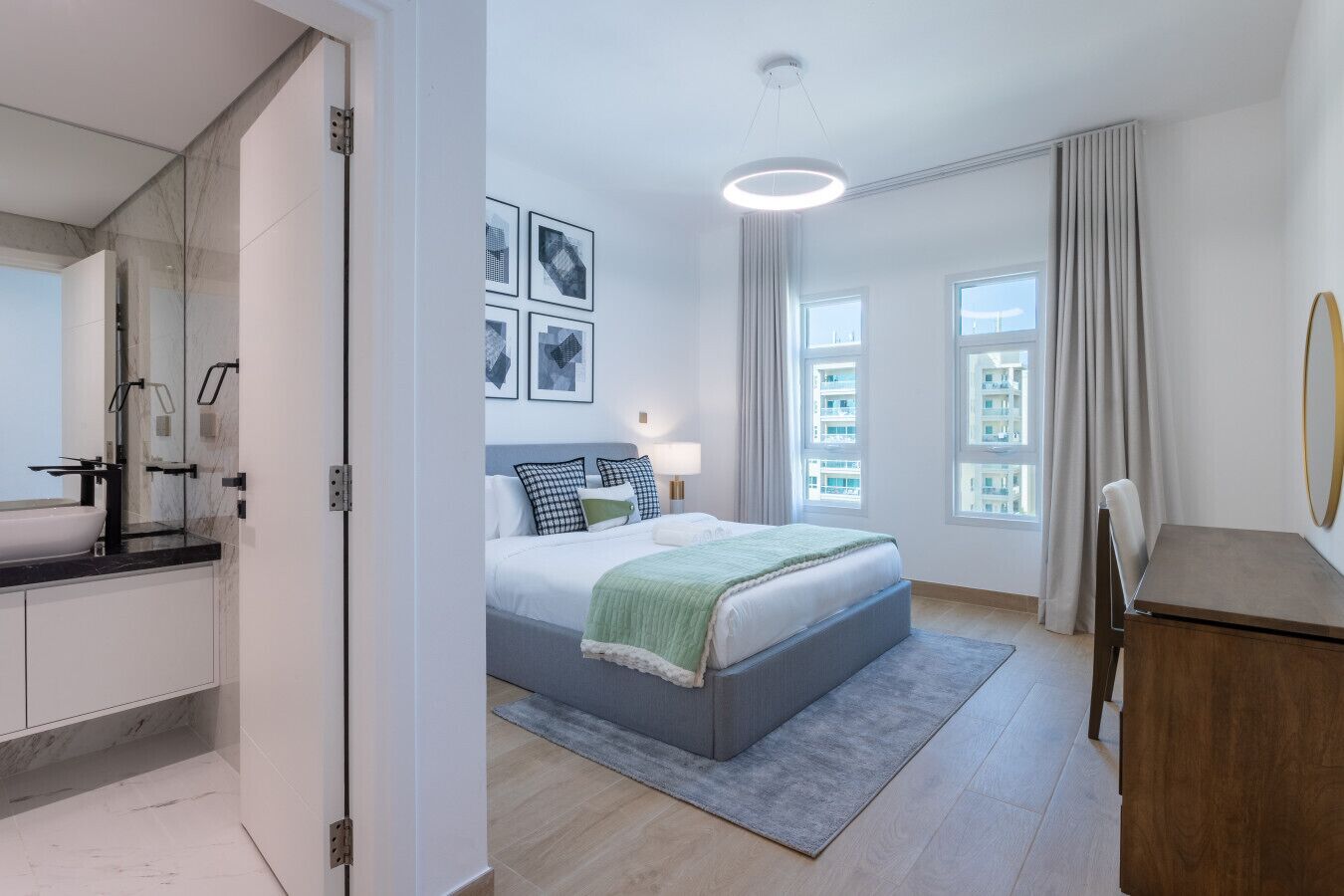 Un dormitorio moderno con una cama grande, una mesita de noche, un escritorio y un baño con lavabo y espejo.