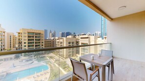 Un balcón con mesa y sillas, con vistas a una piscina y edificios altos.
