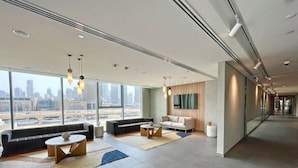 Un espacioso vestíbulo de hotel con diseño moderno, que incluye un área de estar con sofás y mesas, grandes ventanales con vistas a la ciudad y una estética limpia y minimalista.