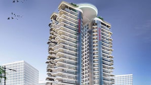 Un immeuble de grande hauteur doté de nombreux balcons, d’une partie supérieure incurvée et d’un ciel dégagé en arrière-plan.