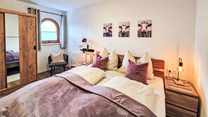 Ein Schlafzimmer mit einem großen Bett, einem Holzschrank, einem Schreibtisch mit Lampe und einem Fenster mit Vorhängen.
