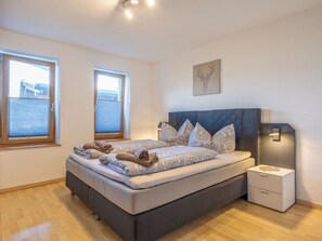 Une chambre à coucher avec un grand lit, deux fenêtres, une table de chevet et une lampe fixée au mur.