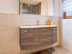 Une salle de bain dotée d’un meuble-lavabo moderne, d’un miroir et d’une fenêtre avec des stores.