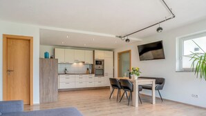 Una cocina moderna con armarios blancos, un comedor con mesa y sillas, y un sofá gris.