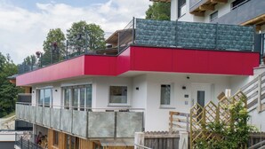 Un edificio moderno de varios pisos con fachada roja y blanca, balcones de madera y una escalera que conduce a un nivel superior.