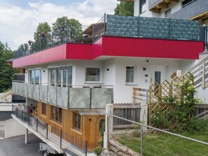 Ein modernes mehrgeschossiges Gebäude mit roter und weißer Fassade, Holzbalkonen und einer Treppe, die zu einer oberen Ebene führt.