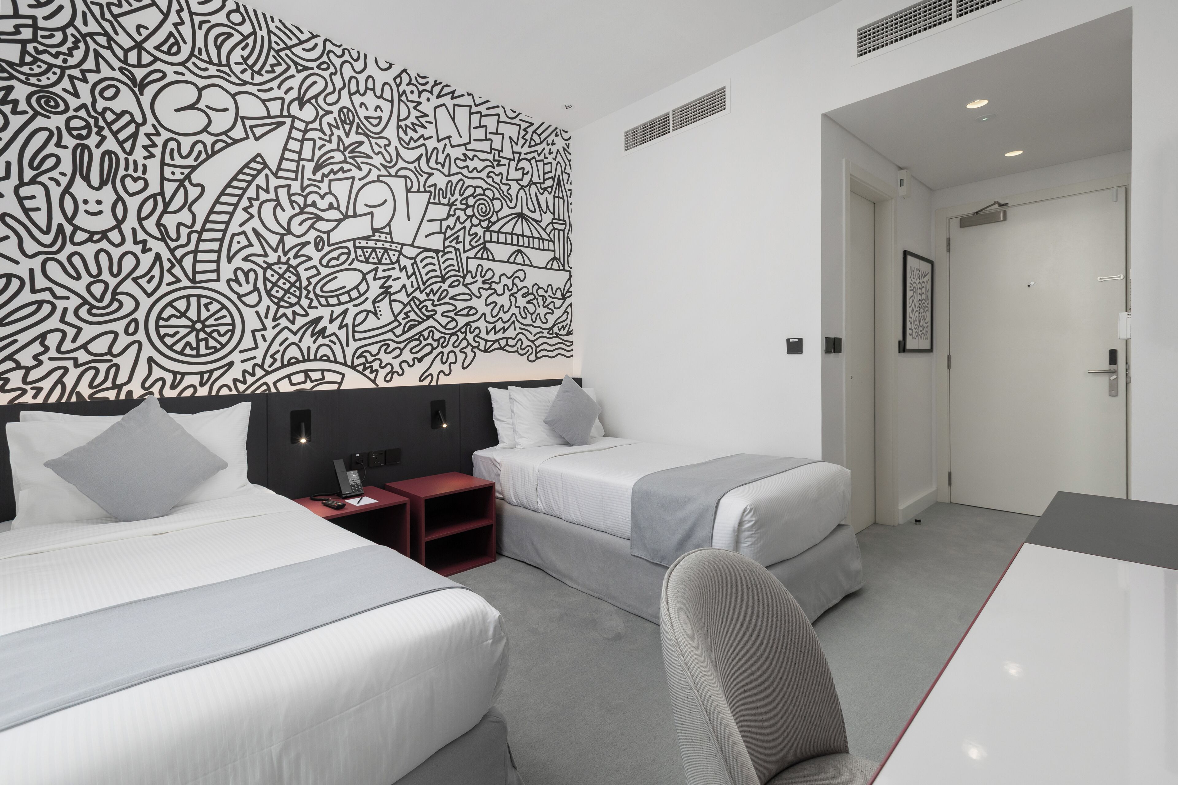 A modern hotel room with two beds, a desk, and a large abstract wall mural.