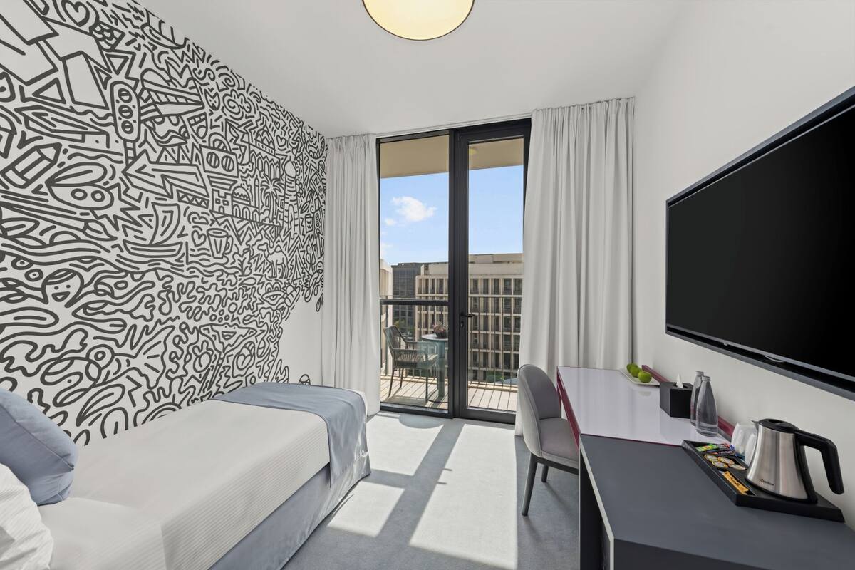Una habitación de hotel moderna con una cama grande, un escritorio con televisor de pantalla plana y un balcón con vistas a la ciudad.