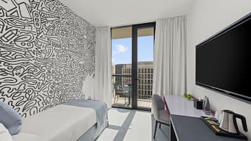 Een moderne hotelkamer met een groot bed, een bureau met een flatscreen televisie en een balkon met uitzicht op de stad.