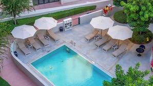 A rooftop pool with lounge chairs and umbrellas, surrounded by greenery and a clear sky. - Nest Hotel, Aljada (Sharjah)