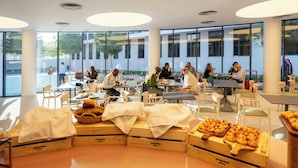 A spacious café with large windows, wooden tables, and chairs, and a variety of pastries displayed on wooden crates. - Nest Hotel, Aljada (Sharjah)