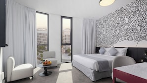 A modern hotel room with a large bed, a sitting area with a table and chair, a small balcony, and a decorative wall. - Nest Hotel, Aljada (Sharjah)