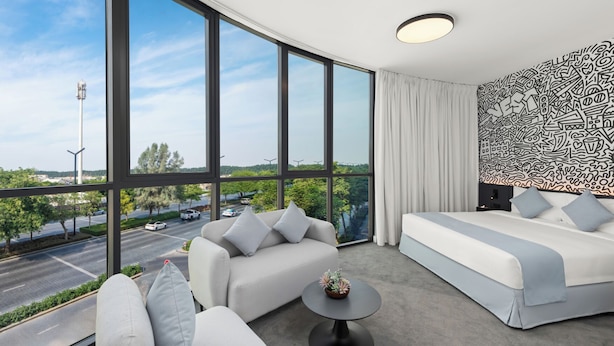 A modern hotel room with large windows, a sofa, a bed, and a small table. - Nest Hotel, Aljada (Sharjah)