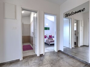 Ein Hotelkorridor mit einem 'Welcome'-Schild, einem Bett mit Kissen und einem Badezimmer mit Dusche.