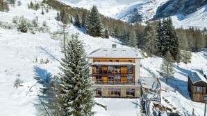 Un moderno lodge de varios pisos con fachada de madera, ventanas amplias y un balcón con vistas a un paisaje montañoso nevado.