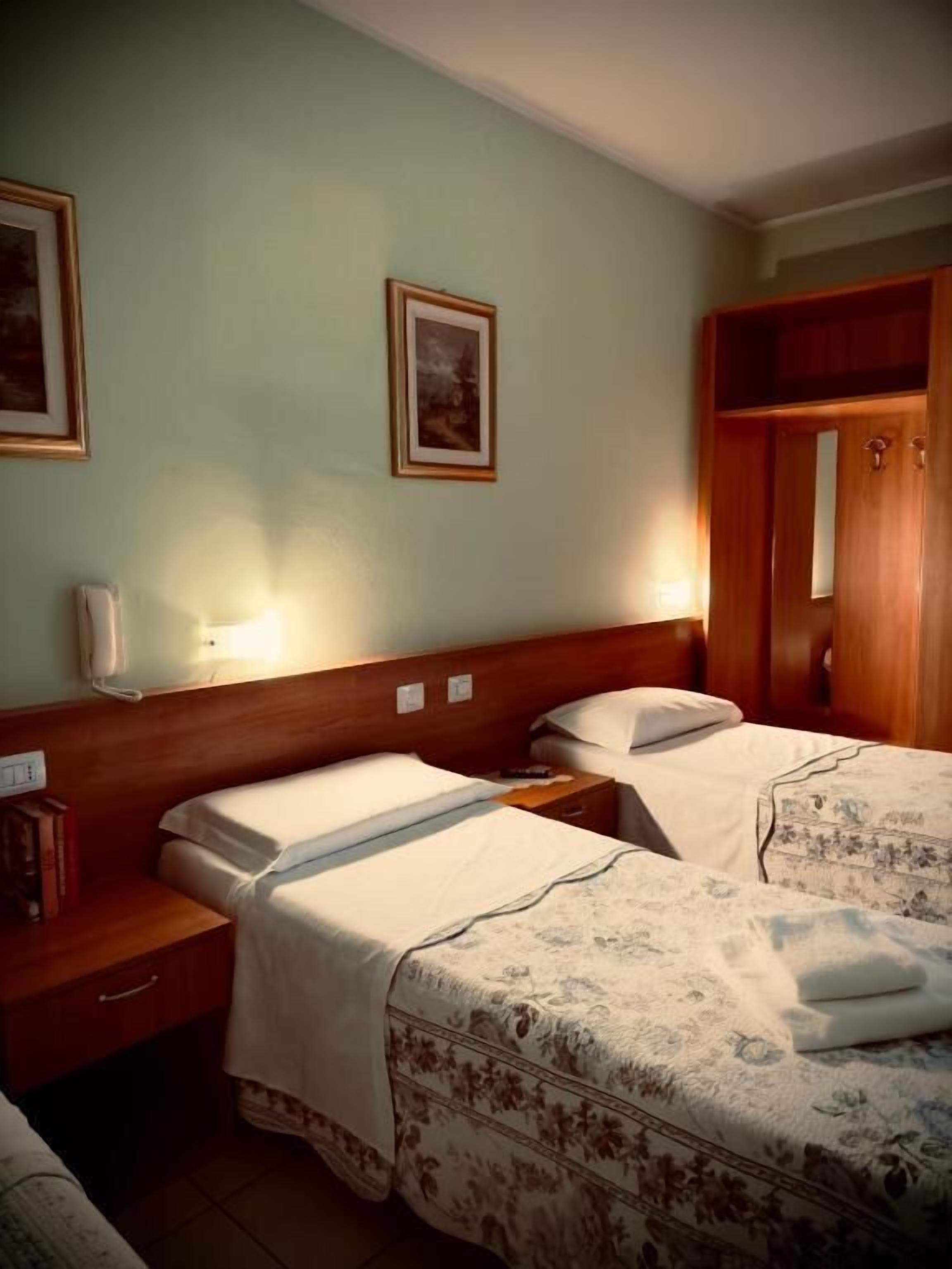 Habitación de hotel con dos camas, cabeceros de madera, una mesita de noche y un armario.
