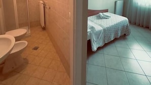 A bathroom with a toilet, shower, and a bed with a white bedspread. - Albergo Trattoria Al Taj (Sevegliano)