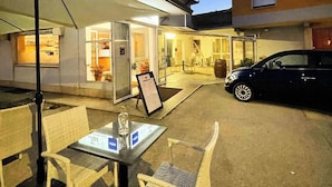 An outdoor seating area with wicker chairs and a table, a car parked nearby, and a building with a sign that reads "Ristorante Trattoria". - Albergo Trattoria Al Taj (Sevegliano)