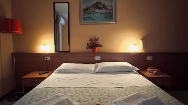 A hotel room with a large bed, two bedside tables, a nightstand, a lamp, a painting on the wall, and a small potted plant. - Albergo Trattoria Al Taj (Sevegliano)