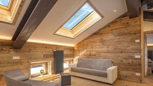 Une pièce de style loft avec un plafond en pente, des murs en bois, un canapé, un fauteuil et un radiateur.