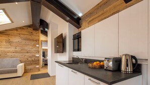 Une cuisine moderne avec des armoires blanches, un comptoir noir et un plafond en bois. On y trouve un grille-pain, une bouilloire et un panier d’oranges sur le comptoir.