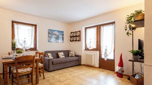 A living room with a dining area, a grey sofa, a small table with chairs, and a red cone decoration. - Lovely apartment for 4 people with WIFI, TV and pets allowed (Isolaccia)