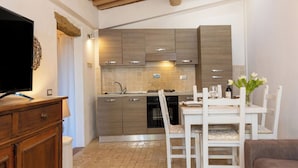 A modern kitchen with wooden cabinets, a dining table with chairs, and a TV on a wooden cabinet.