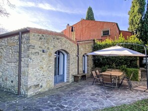 Un bâtiment en pierre avec une porte bleue, une terrasse avec une table et des chaises, et un parasol.