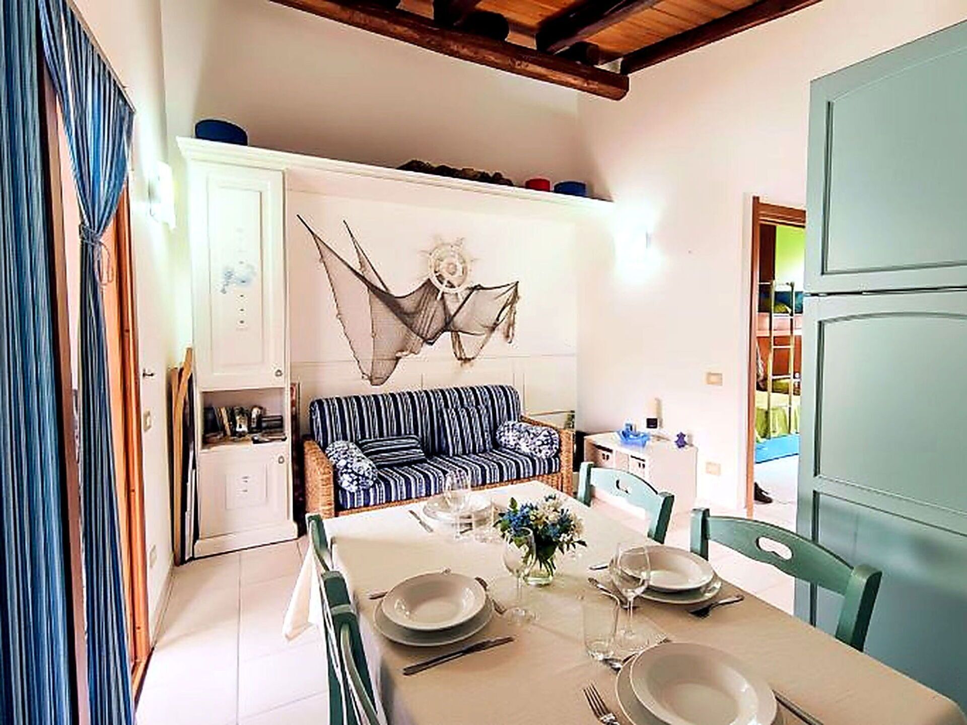 A dining area with a table set for four, a striped sofa, and a decorative wall hanging.