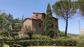 Edificio de piedra con balcón, rodeado de follaje y árboles.