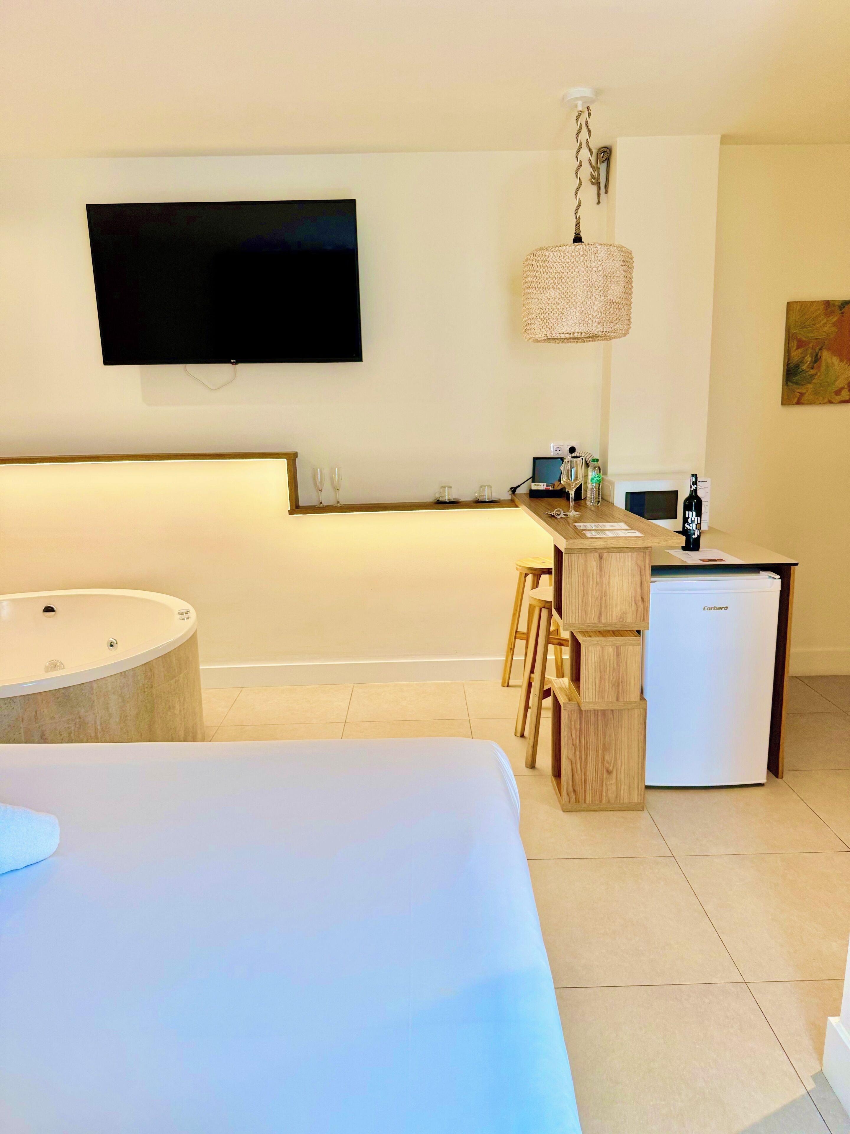 Una habitación de hotel moderna con una cama grande, una kitchenette pequeña, un televisor montado en la pared y una zona de bar de madera.
