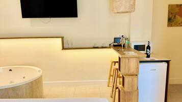Una habitación de hotel moderna con una cama grande, una kitchenette pequeña, un televisor montado en la pared y una zona de bar de madera.