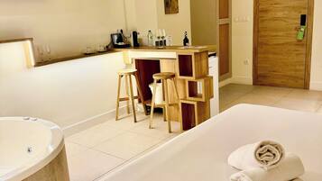 Ein modernes Hotelzimmer mit einem großen Bett, einer separaten Sitzecke mit Tisch und Stühlen, einem integrierten Schreibtisch, einer großzügigen Badewanne und einem an der Wand montierten Flachbildfernseher.