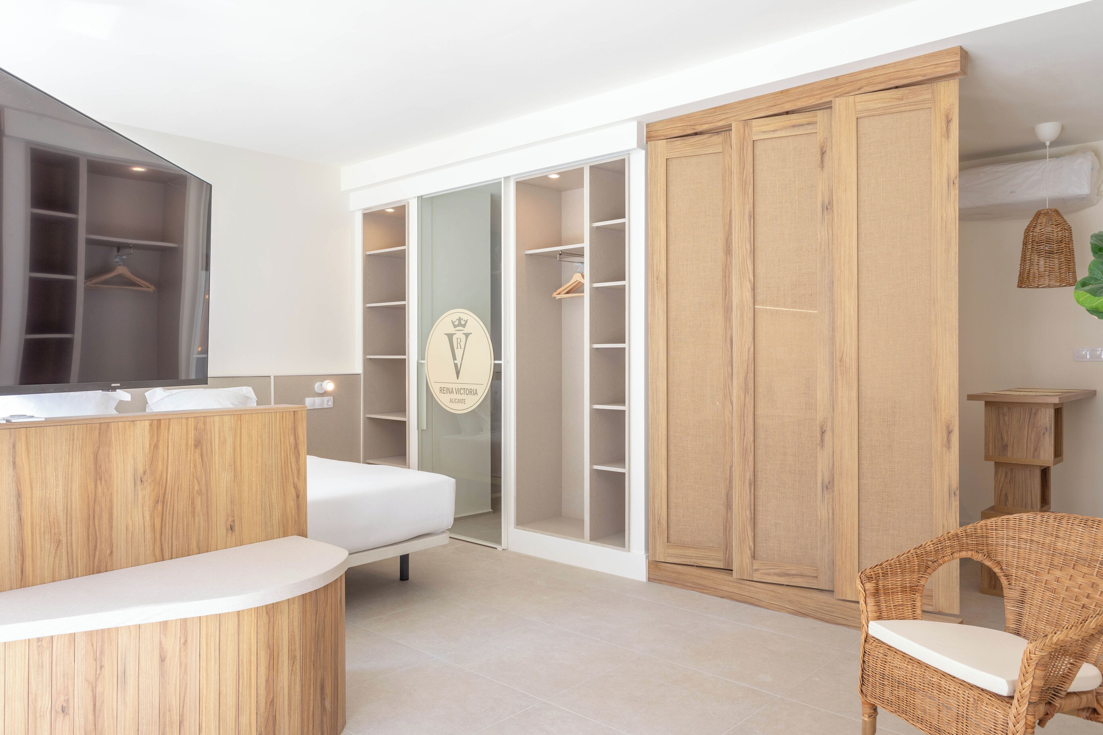 Un dormitorio moderno con una cama, un armario de madera, una silla de mimbre y un tocador con espejo.