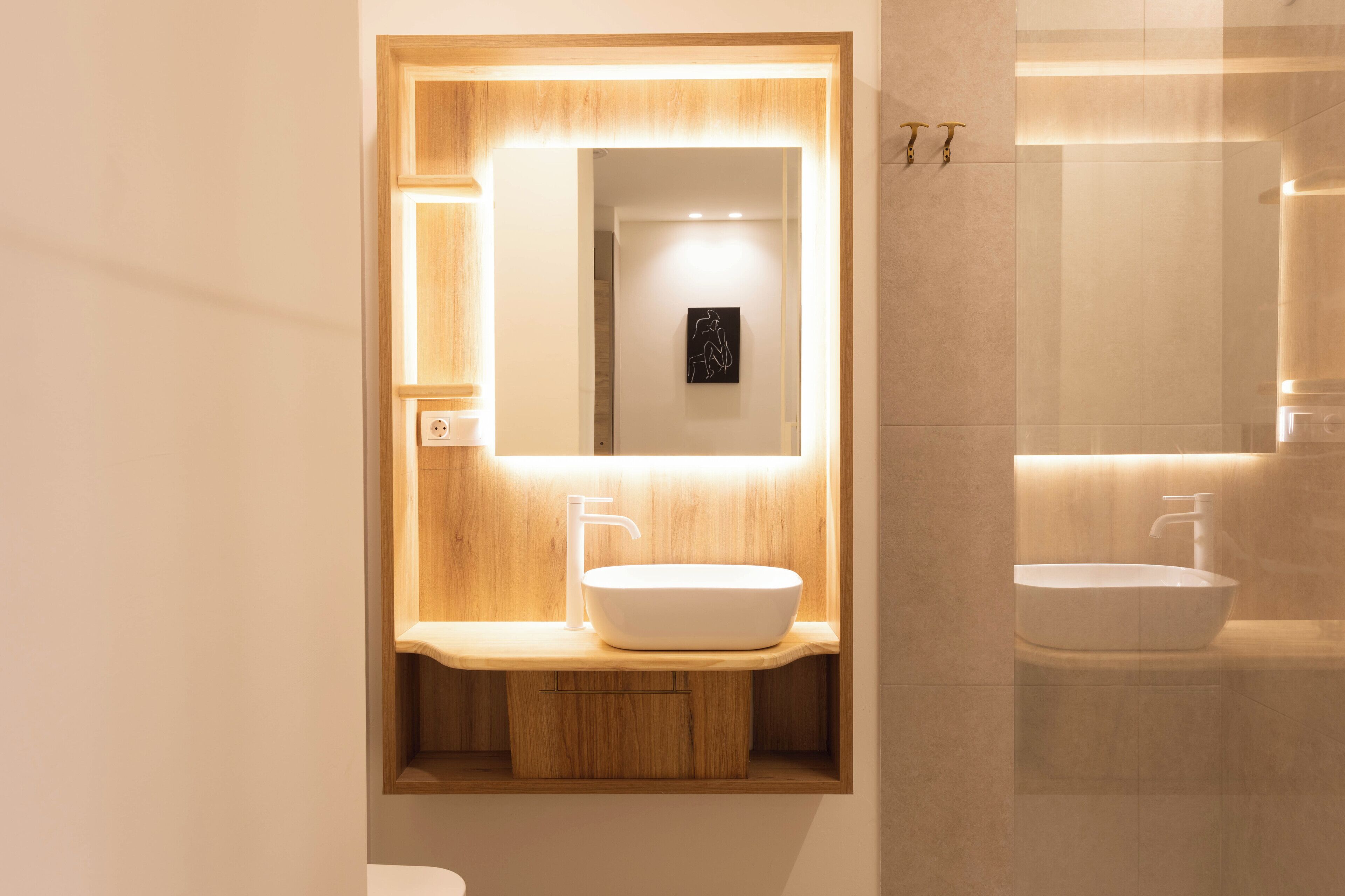 A modern bathroom with a wooden vanity, a large mirror, and a white sink.