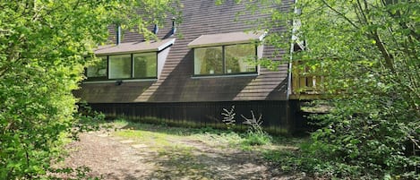 A modern house with a sloped roof, large windows, and a dirt path leading to the entrance.