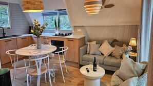 A modern kitchen with a dining area, a sofa, and a coffee table with a bottle and glasses. - Comfortable Chalet near Durbuy Center (Durbuy)
