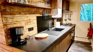 A modern kitchen with wooden paneling, a coffee maker, a sink, and a window with a view of trees. - Elegant Chalet Getaway in Ardennes (Durbuy)