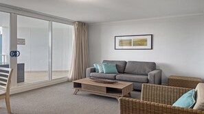 A modern living room with a grey sofa, two teal cushions, a wooden coffee table, and wicker chairs. - Ocean Jewel, TOP NOTCH (ETTALONG BEQCH)