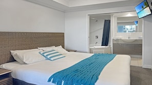 A hotel room with a bed, a bathroom with a sink and mirror, and a TV mounted on the wall. - Ocean Jewel, TOP NOTCH (ETTALONG BEQCH)