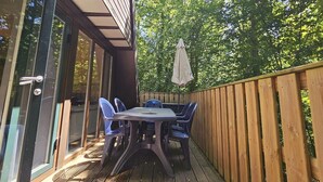 An outdoor deck with a table and chairs, a wooden fence, and a large umbrella. - Renovated Ardennes Chalet with Patio (Durbuy)